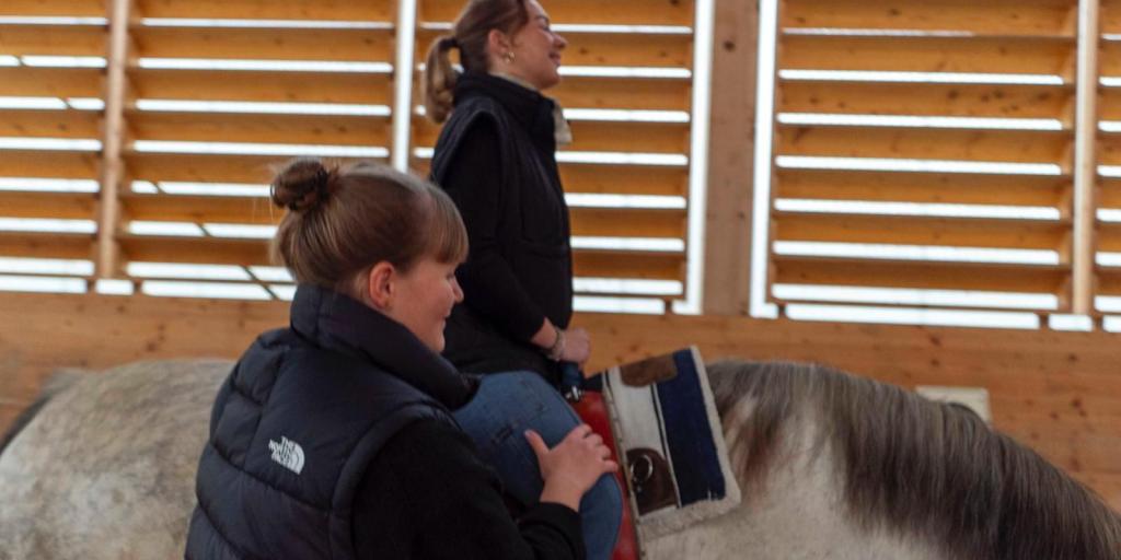 Man sieht ein kleines Mädchen auf einem Pferd, begleitet von einer Frau. Dies ist ein Ausschnitt von einer Hippotherapie.